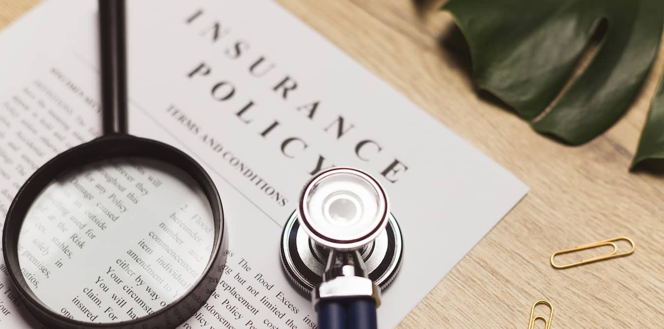 Sethoscope and magnifying glass on top of insurance policy.