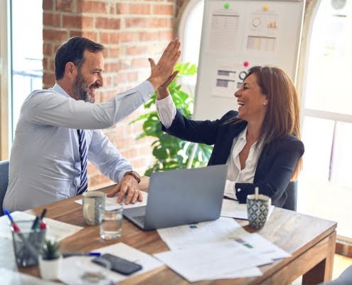 Two employees giving a high five at a desk.