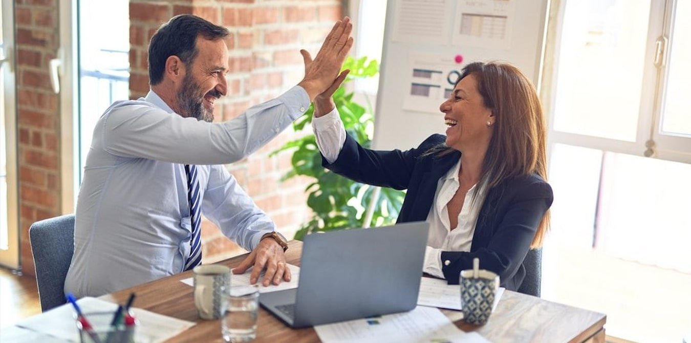 Two employees giving a high five at a desk.